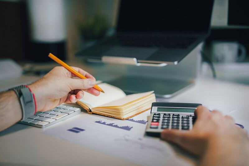 Manos con una calculadora, un cuaderno y un lápiz revisando un presupuesto mensual