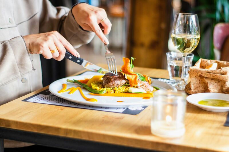 Una persona cenando un plato servido con una copa de vino blanco sobre una mesa de madera