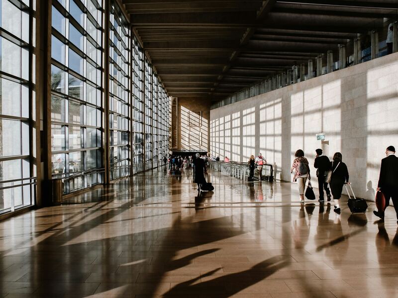 Viajeros con maletas caminando por una terminal de aeropuerto luminosa y soleada