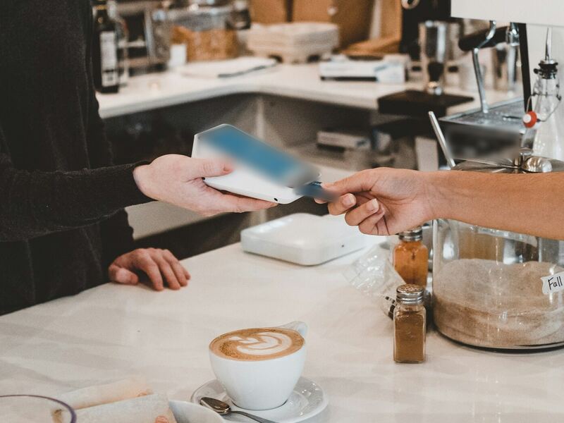 Un cliente entrega una tarjeta a un barista en la barra de un café junto a un latte recién hecho
