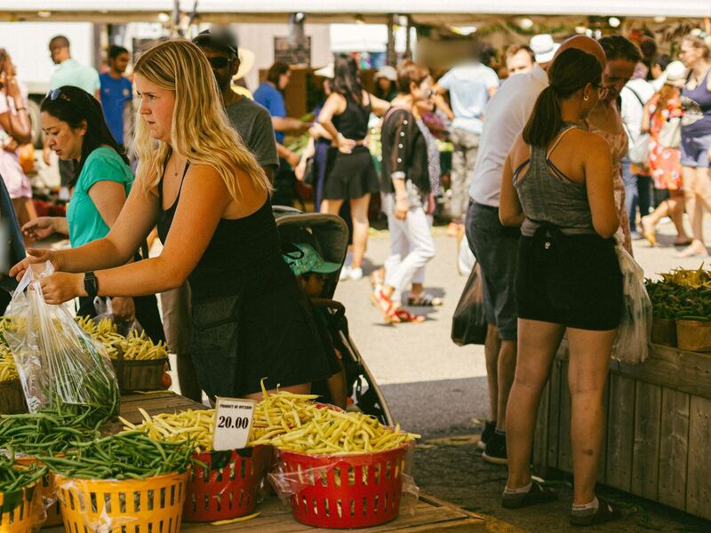Personas eligiendo ejotes verdes y amarillos en un concurrido mercado al aire libre