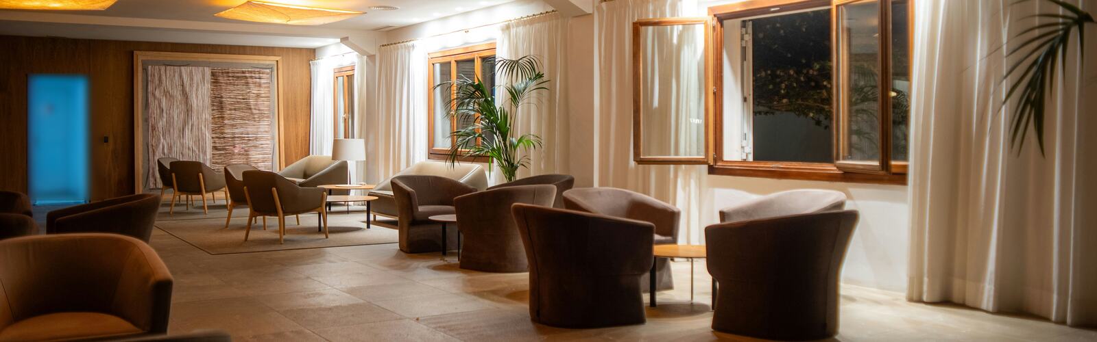 Una sala tranquila con sillones, cortinas largas y luz cálida al anochecer