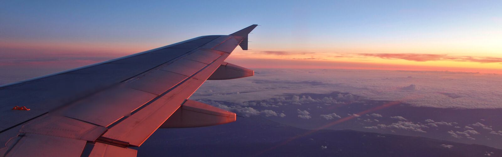 View from a plane window of the wing over the clouds at sunset
